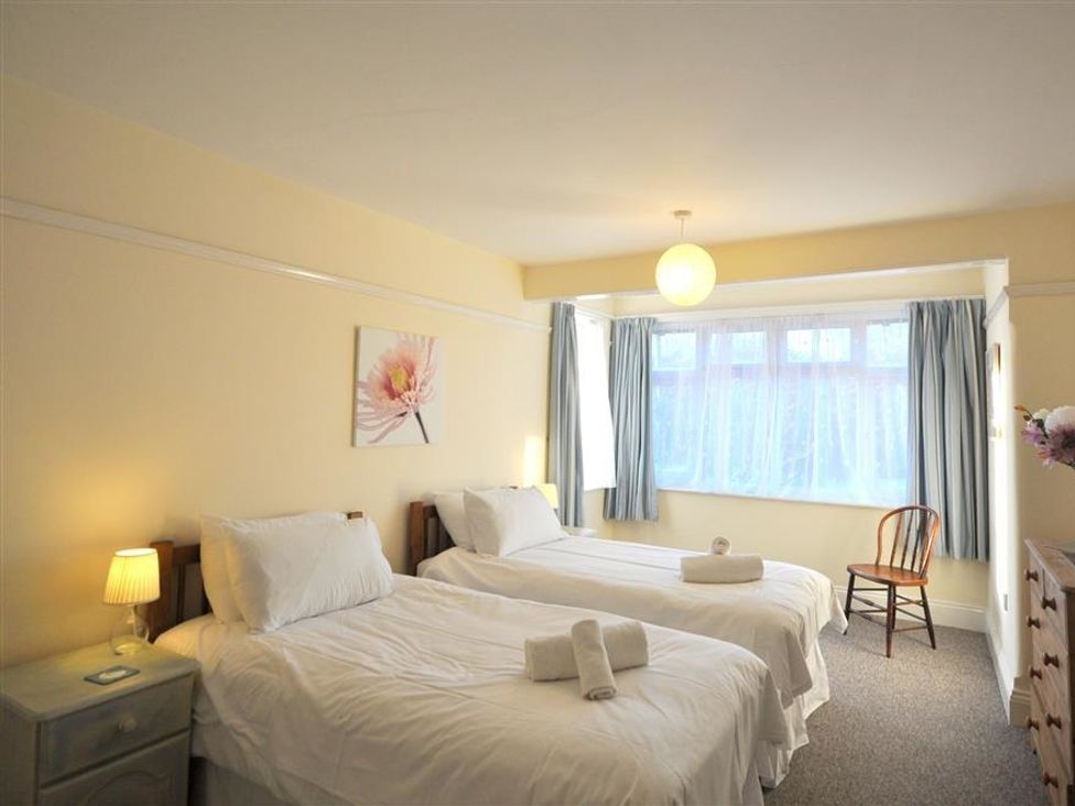 A bedroom with two single beds a bedside table with lamp a wooden chair and a window with curtains at Rainbow's End in Cove Castle