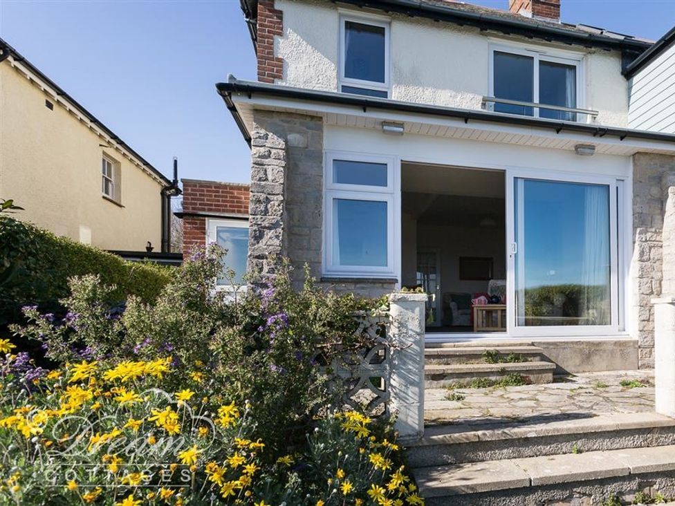 Exterior view of a two-story house with stone and brick walls with a patio and yellow flowers at Rainbow's End in Cove Castle