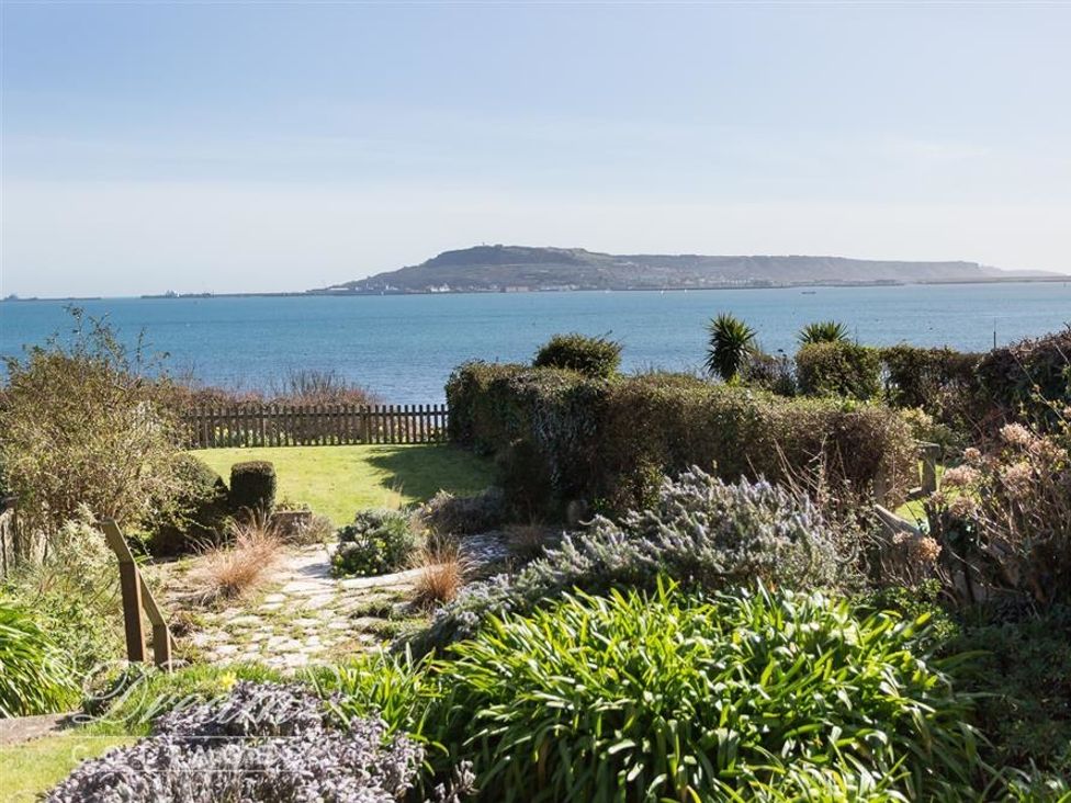 A garden with bushes and plants overlooking the sea with a mountain in the distance at Rainbow's End in Cove Castle