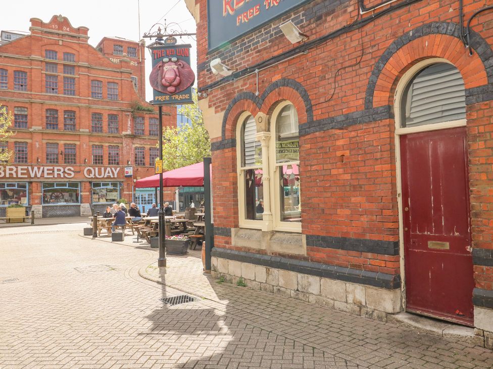 An outdoor seating area with people sitting at wooden picnic tables next to a red brick building with arched windows and a red door at Brewers Quay harbour