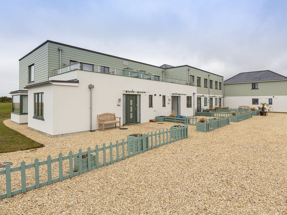 A modern two-story building with small fenced garden areas and a bench outside at 3 Ocean Reach in Bolberry