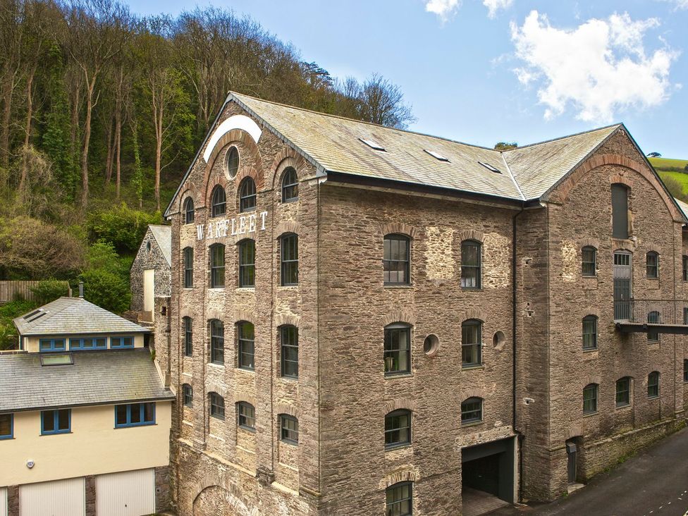 A large stone building with multiple windows and the name warfleet on the side near trees and smaller buildings at 8 The Pottery in Dartmouth