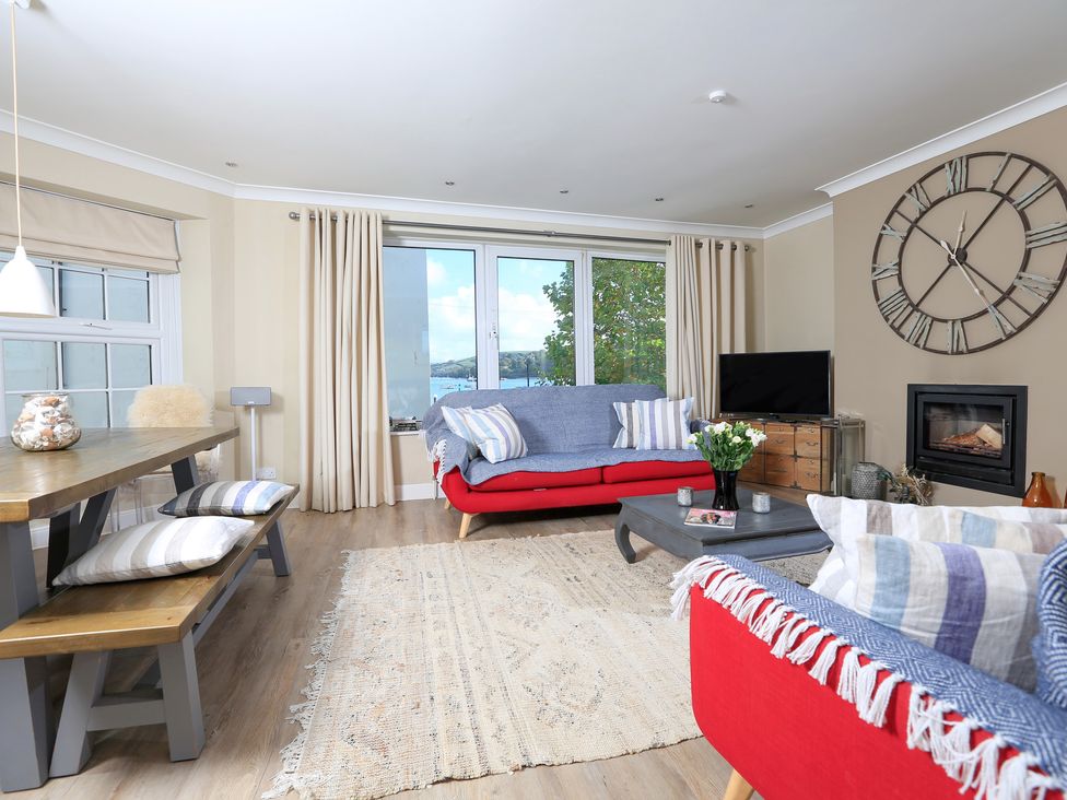 A living room with red sofas, a wooden dining table with benches, a wall clock, and a fireplace at Normandy Watch in Salcombe