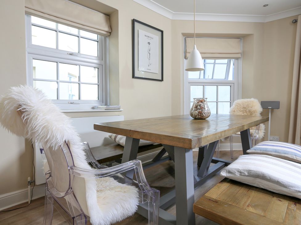 A dining area with a wooden table multiple chairs and windows at Normandy Watch in Salcombe
