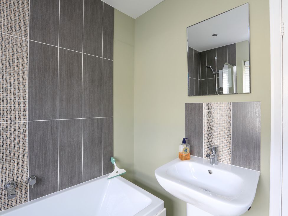 A bathroom with a bathtub a sink a mirror and tiled wall sections at Normandy Watch in Salcombe