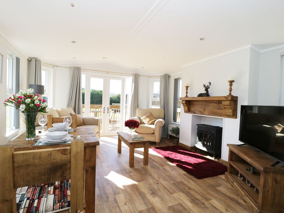 A living room with wooden furniture a fireplace armchairs and a dining table at Beech Tree Lodge in Stamford Bridge