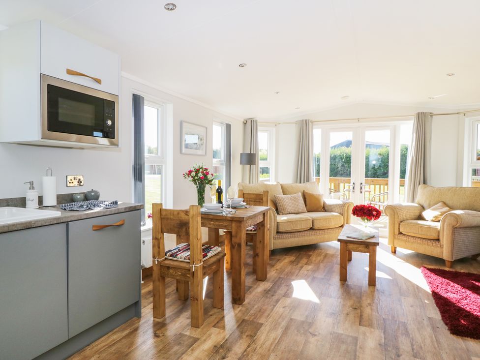 A living room with sofas a wooden dining table kitchen cabinets and a coffee table with flowers at Beech Tree Lodge in Stamford Bridge
