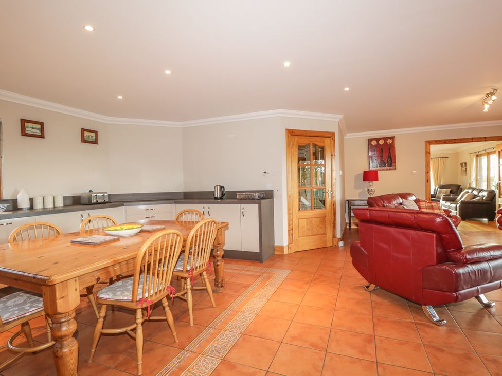 A kitchen dining area with wooden table and chairs next to red leather sofas at The Glebe in Invergordon