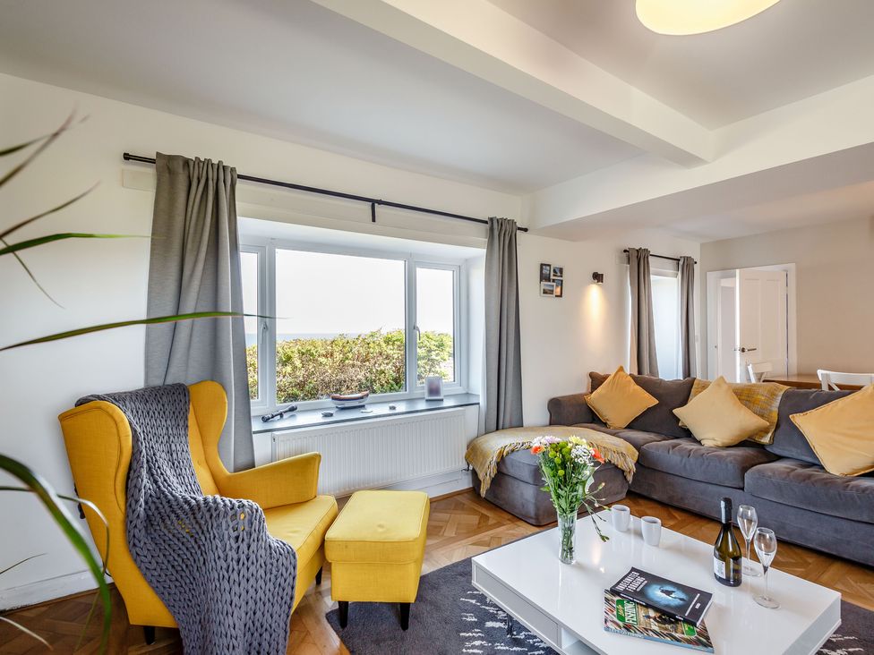 A living room with a yellow armchair and gray sofa with yellow cushions at Tyn Y Berth in Benllech