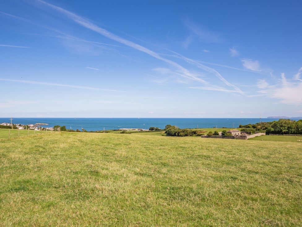 A grassy field with a stone building near the coast and blue ocean in the background at Tyn Y Berth in Benllech