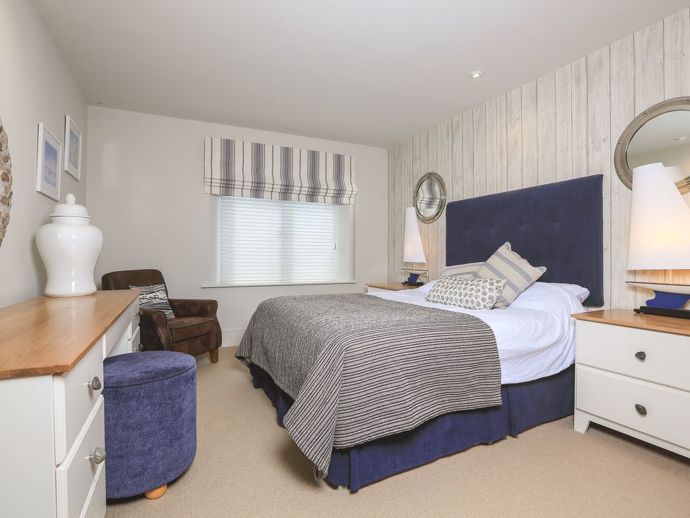 A bedroom with a bed blue headboard side tables with lamps a chair dresser and a window at Quayside Dart Marina in Dartmouth