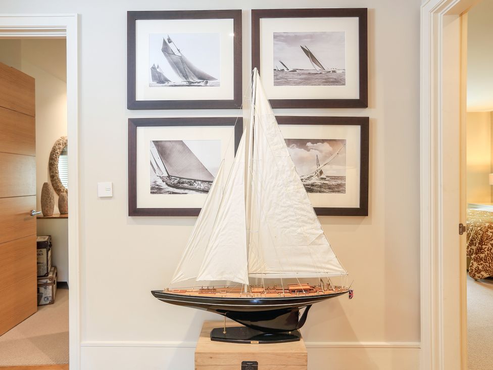 A model sailboat on a wooden stand between two doorways with four framed black and white sailboat pictures on the wall at Quayside Dart Marina in Dartmouth
