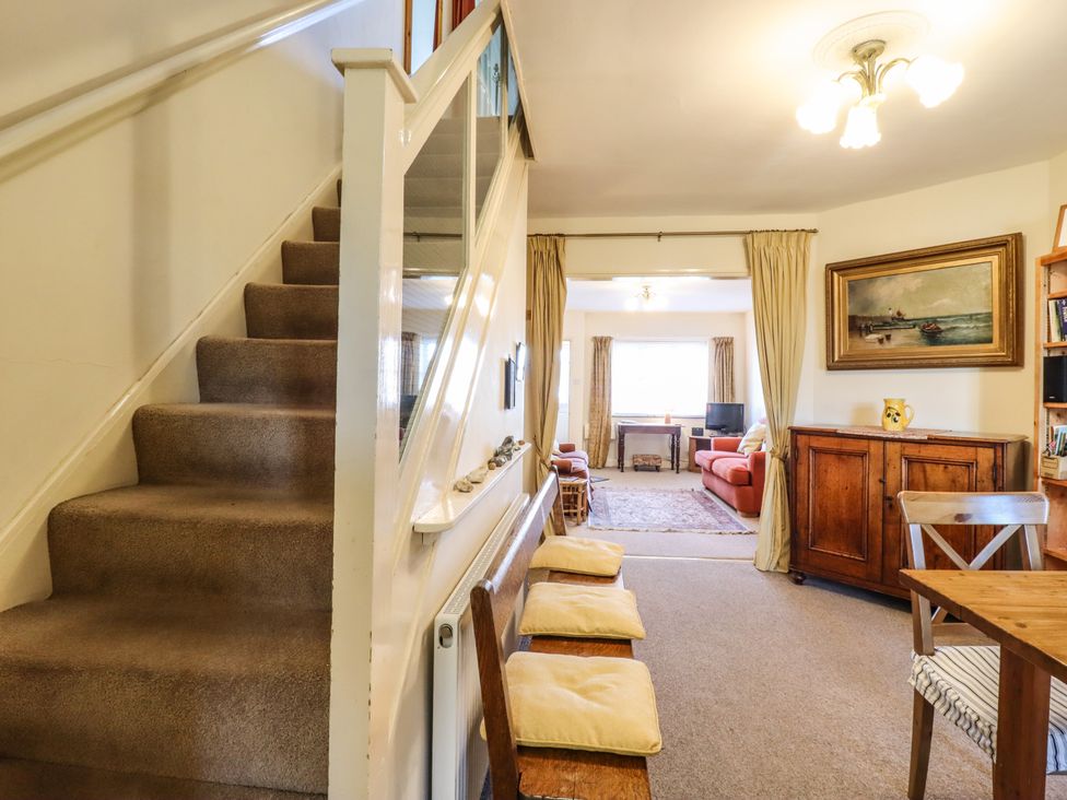 A carpeted staircase next to a hallway with a wooden bench and cushions leading to a sitting room with sofas and a wooden cabinet at La Plage in Walmer