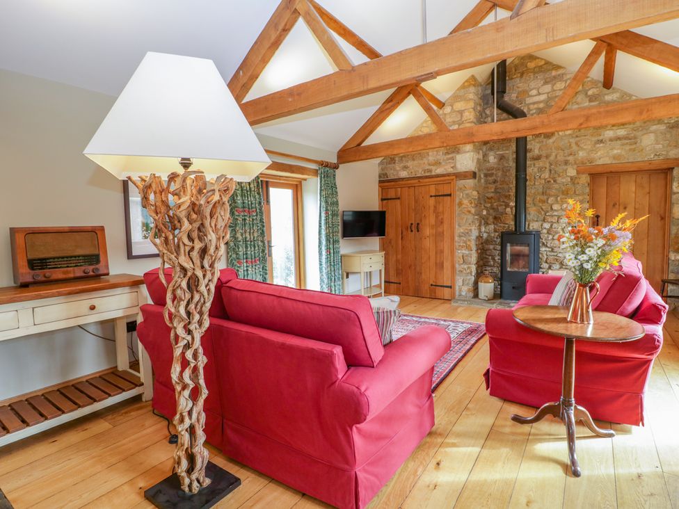 A living room with wooden beams red sofas a floor lamp wooden table and a stone fireplace at Middle Farm Annex in Long Bredy