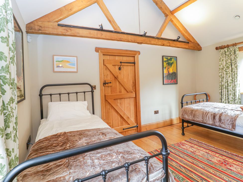 A bedroom with two single beds with metal frames wooden door wooden beams and patterned rug at Middle Farm Annex in Long Bredy