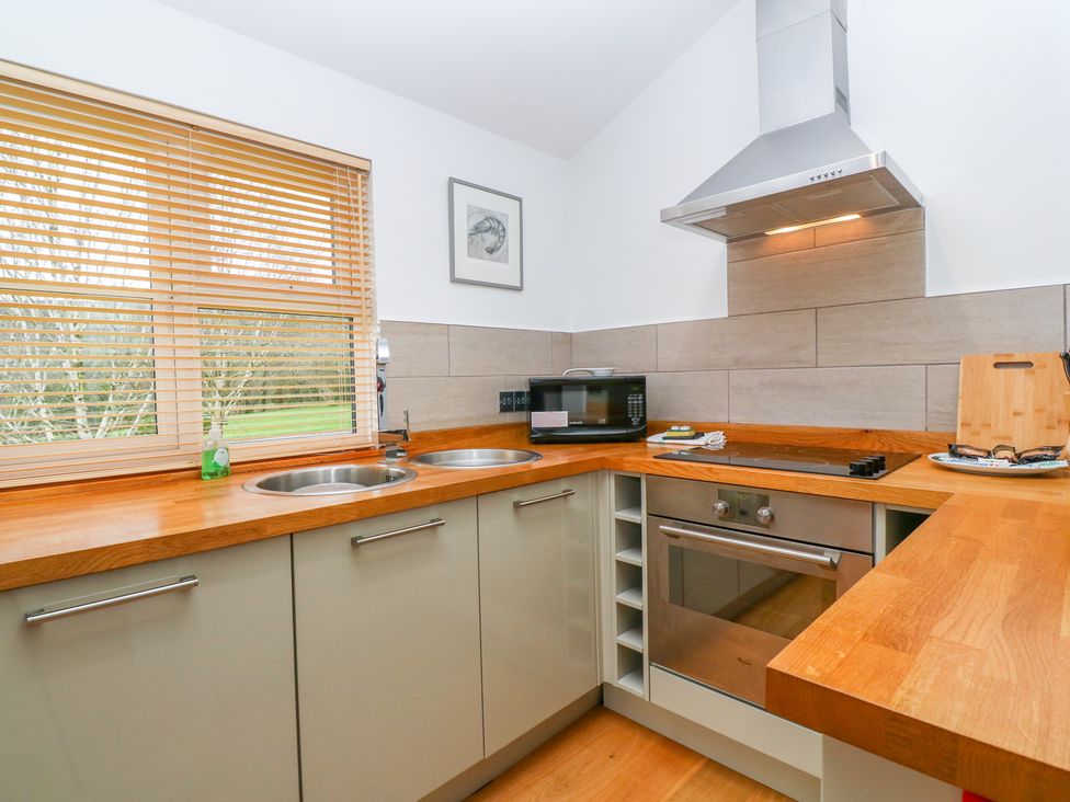 A kitchen with wooden countertops a double sink a microwave an oven and stove with a stainless steel hood and a window with wooden blinds at 1 Lake View in Lanreath