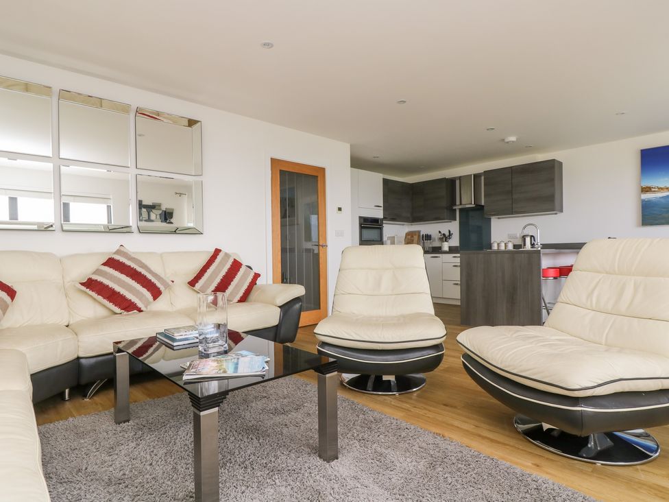 A living room with cream sofas red striped cushions a glass coffee table and an open kitchen in the background at Praa Waves in Praa Sands